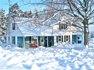 a house including its front porch and surrounding trees, all covered in snow